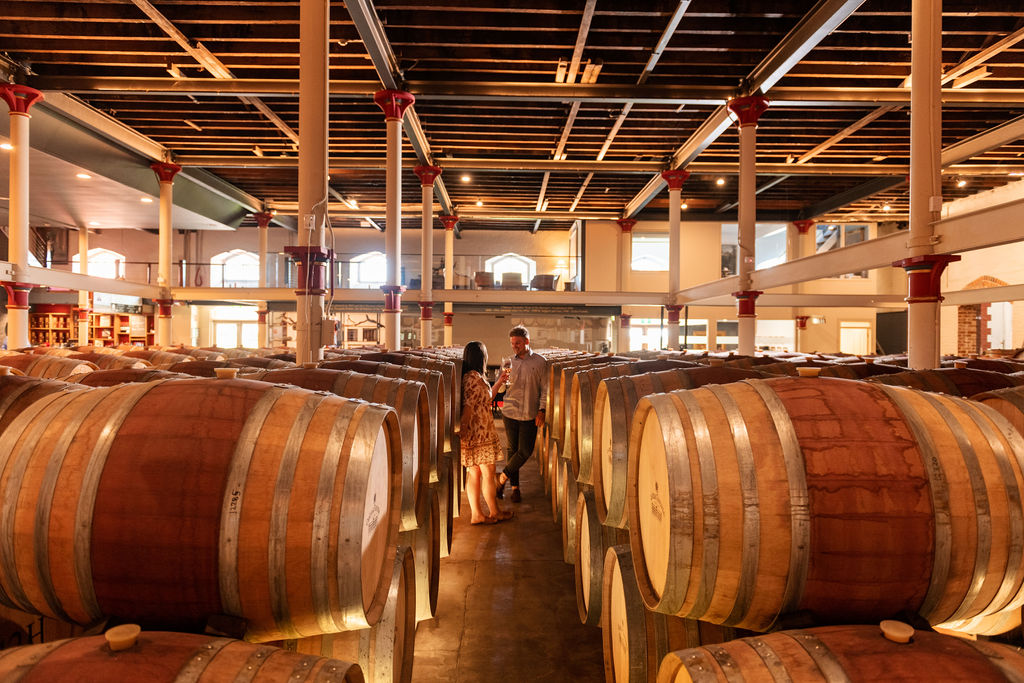A man and a woman drinking wine inside the winery among barrels
